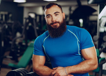 有胡子的年轻的<strong>男人</strong>。健美运动员蓝色的t恤站健身房