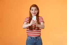逗乐兴奋红色头发的人女记录视频激动著名的人微笑惊讶持有智能手机采取图片旅游喜欢旅行拍摄夏天旅程橙色背景