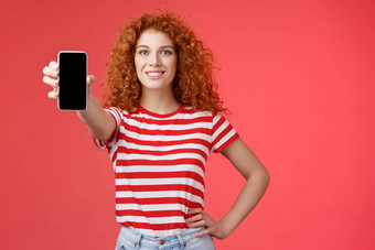 自信好看的红色头发的人卷曲的女人现在很酷的应用程序持有智能手机扩展手显示电话屏幕微笑自信的推荐订阅博客社交媒体