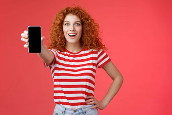 快乐的有吸引力的有魅力的欧洲红色<strong>头</strong>发的人女孩卷曲的发型显示智能手机屏幕微笑幸福的促进应用程序建议推荐好应用程序社会媒体<strong>页</strong>面红色的<strong>背景</strong>