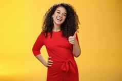 肖像快乐乐观年轻的卷发女人红色的衣服笑快乐显示拇指批准手势很高兴太棒了的想法接受计划黄色的墙