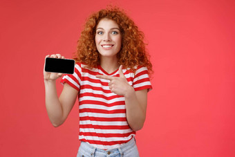 兴奋快乐好看的欧洲红色头发的人卷曲的女孩惊讶显示个人成就分数智能手机游戏显示电话屏幕指出显示讨论太棒了游戏微笑很高兴