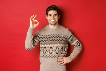概念圣诞节庆祝活动冬天假期生活方式肖像有吸引力的男人。圣诞节毛衣微笑快乐显示标志赞美好红色的背景