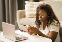 非洲女人白色t恤坐着地板上发短信消息智能手机移动PC特写镜头沙发上背景