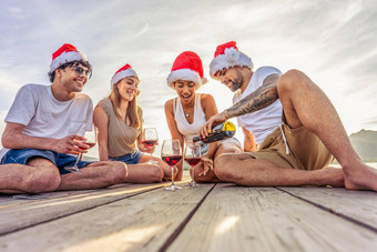 快乐人享受户外生活异国情调的假期度假胜地喝酒精集团年轻的朋友有趣的日落穿红色的圣诞老人老人他坐着码头海假期度假胜地