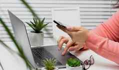 女人坐在白色表格持有智能手机手手类型移动PC键盘在线购物自由远程办公办公室