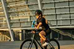 专业女骑自行车的人黑色的骑自行车服装保护齿轮持有水瓶骑自行车城市培训在户外日落