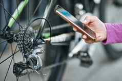 关闭拍摄手女骑自行车的人持有智能手机检查自行车机制链轮链山自行车在户外白天