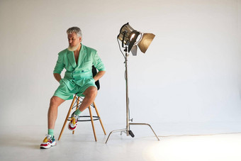 工作室拍摄时尚的灰色的头发的中间岁的男人。穿时尚的装色彩斑斓的运动鞋坐着工作室关注的焦点摆姿势白色背景