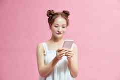 美丽的亚洲女孩移动电话闲谈，聊天应用程序微笑站粉红色的背景