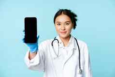 网络医疗医生概念微笑亚洲医生显示移动电话屏幕站诊所统一的蓝色的背景