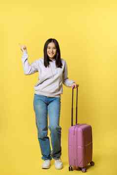 完整的长度拍摄微笑亚洲旅游女孩旅行者指出促销广告站手提箱假期黄色的背景