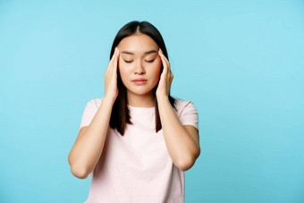 亚洲女孩<strong>摩擦</strong>按摩头手指关闭眼睛按摩头疼偏头痛站蓝色的背景