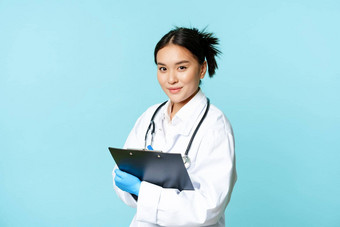 医疗保健诊所概念微笑朝鲜文医生女人医生医疗统一的持有剪贴板站蓝色的背景