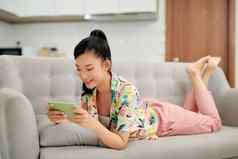 微笑年轻的亚洲女人移动电话应用程序玩游戏放松沙发