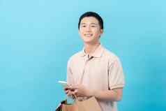 年轻的亚洲男人。购物袋移动电话微笑购物蓝色的背灌