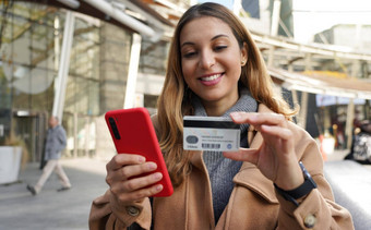 快乐微笑女人持有智能手机进入信贷卡数量冬天季节在户外