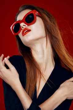 漂亮的女人穿太阳镜时尚摆姿势发型红色的背景