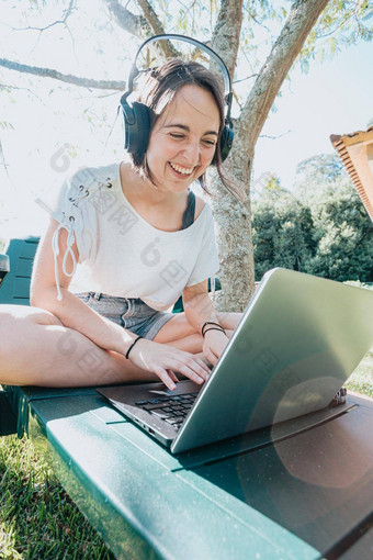 年轻的女人坐着花园微笑研究大学<strong>享受</strong>户外娱乐听力音乐移动PC房子研究<strong>人生</strong>活方式概念打字电脑