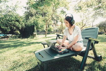 年轻的女人坐着花园微笑研究大学享受户外娱乐听力音乐移动PC复制空间人生活方式概念打字电脑