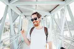 肖像年轻的男人。机场公共汽车站行李袋手提箱持有地图微笑赶时髦的人旅行者太阳镜复制空间阳光明媚的一天