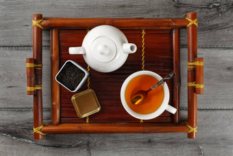表格前视图白色陶瓷<strong>茶壶</strong>杯热黑色的茶银勺子打开剂量宽松的叶茶服务竹子托盘灰色的木桌子上