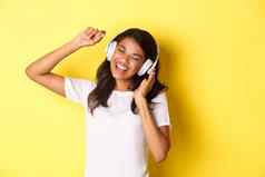 快乐的十几岁的非裔美国人女孩听音乐耳机跳舞乐观的唱歌站黄色的背景