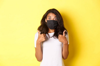 概念冠状病毒流感大流行生活方式肖像美丽的非裔美国人女孩黑色的脸面具显示竖起大拇指惊讶推荐黄色的背景