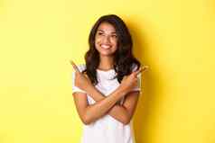 肖像有吸引力的非裔美国人女孩白色t恤微笑左指出手指横盘整理使选择提供了站黄色的背景