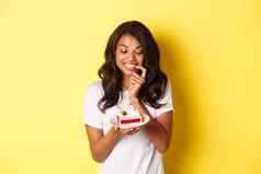 图像美丽的非裔美国人女人诱惑微笑美味的一块蛋糕站黄色的背景