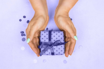 女人的手蓝色的柔和的修指甲持有礼物弓紫色的背景仙女概念假期礼物惊喜生日一年圣诞节