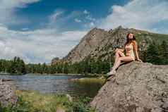 旅游女孩享受神奇的视图湖松柏科的森林神奇的视图坐着大石头海岸绿松石湖山徒步旅行自然公园可爱的女孩旅游坐着大石头湖水清晰的石头可见水
