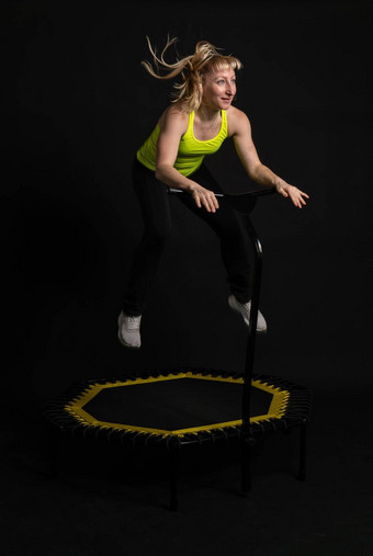 女孩健身蹦床黑色的背景黄色的t恤蹦床适合活跃的身体健康的运动可爱的俱乐部人白色教练物理<strong>肌肉</strong>教练享受
