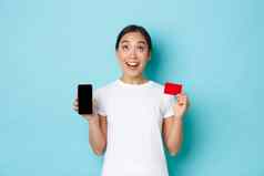 电子商务购物生活方式概念兴奋惊讶亚洲女孩发现太棒了应用程序在线购物订单跟踪持有移动电话显示屏幕信贷卡