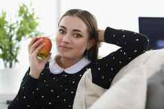 漂亮的年轻的女人坐舒服的沙发上首页新鲜的苹果水果零食