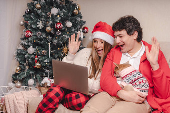 肖像可爱的夫妇丈夫妻子移动PC红色的圣诞老人他视频调用闲谈，聊天小狗狗毛衣享受圣诞节时间首页在线问候