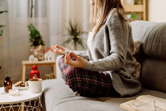 舒适的女人针织冬天温暖的毛衣网纹睡衣喝热可可咖啡杯子阅读书冥想瑜伽沙发上首页圣诞节假期装饰灯