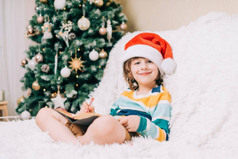 微笑孩子男孩红色的圣诞老人他坐沙发上写作信亲爱的圣诞老人首页孩子列表梦想圣诞节礼物快乐圣诞节快乐一年