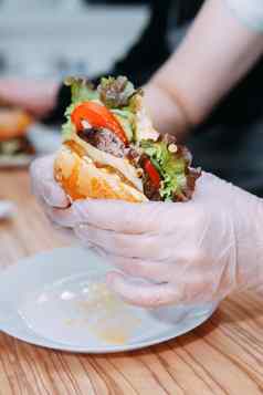 戴着手套手持有汉堡吃汉堡牛肉蔬菜美味的汉堡包烹饪主类汉堡洋葱酱汁