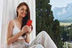 快乐的女人坐着阳台电话美丽的山视图夏天放松概念