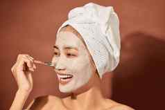 年轻的美丽的女人粘土面具脸沙龙皮肤护理自然奶油藻类