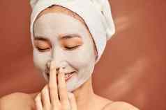 美丽的亚洲女人应用面部面具脸皮肤护理治疗水疗中心自然美美容概念