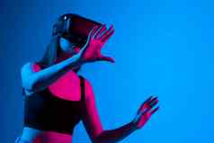 年轻的女人穿虚拟现实设备霓虹灯光蓝色的背景
