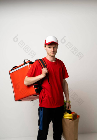 交付男人。红色的统一的热袋肩膀持有纸袋食品杂货食物交付服务