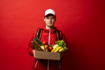年轻的交付男人。携带纸盒子袋杂货店食物喝商店孤立的红色的工作室背景复制空间交付概念