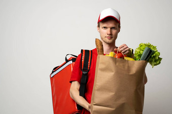 交付概念肖像很高兴交付男人。红色的统一的微笑携带纸袋食物产品孤立的白色背景食物交付服务
