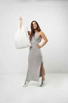 浅黑肤色的女人女人灰色衣服持有棉花购物者袋蔬菜产品白色房间生态友好的购物袋浪费塑料免费的概念