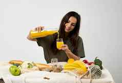 女人绿色t恤倒汁玻璃瓶玻璃表格网生态袋健康的素食主义者蔬菜水果面包零食浪费概念