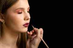 化妆艺术家适用于红色的口红美丽的女人脸手化妆主绘画嘴唇年轻的美模型女孩使过程