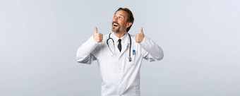 科维德冠状病毒爆发医疗保健工人流感大流行概念热情的英俊的医生白色外套前左广告竖起大拇指推荐产品